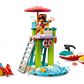 The LEGO® Friends Beach Water Scooter set from Legos - Toyhouse includes a lifeguard tower with a figure using binoculars, a crab, and a boat. Another figure is near a sandcastle with a spade and lifebuoy as the water scooter zooms past under an umbrella.