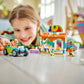 A child is deeply engaged on the floor, creatively building with toy blocks and zooming a small car around their imaginative landscape, reminiscent of a LEGO Friends adventure. Nearby, they pretend to run a beach smoothie stand using their LEGO® Friends Beach Smoothie Stand from Legos - Toyhouse playset, blending fun and creativity seamlessly.