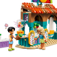 Two toy figures are positioned in front of the lively LEGO® Friends Beach Smoothie Stand from Legos - Toyhouse, featuring a playful food set with a blender and smoothies surrounded by colorful building blocks.