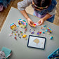 A child builds with colorful pieces from the LEGO® Friends Heartlake City Candy Store by Legos - Toyhouse, following digital instructions on a tablet.