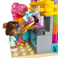 Two LEGO minifigures stand outside the vibrant LEGO® Friends Heartlake City Candy Store by Legos - Toyhouse, with one holding tongs near a swirling pink treat—ideal for shop toy fans and creative builders.