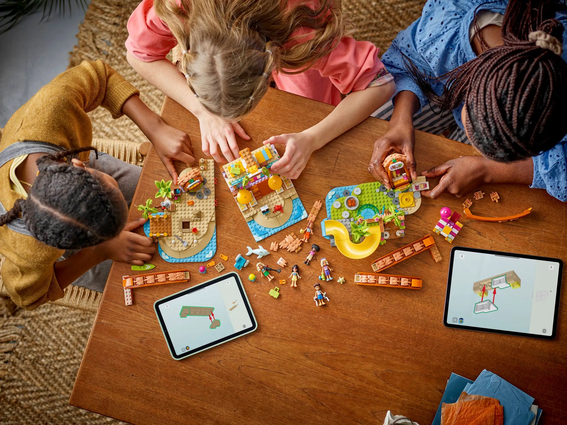 Three children build the LEGO® Friends Family Vacation Beach Resort set by Legos - Toyhouse on a wooden table, using instructions displayed on two tablets amid scattered pieces.