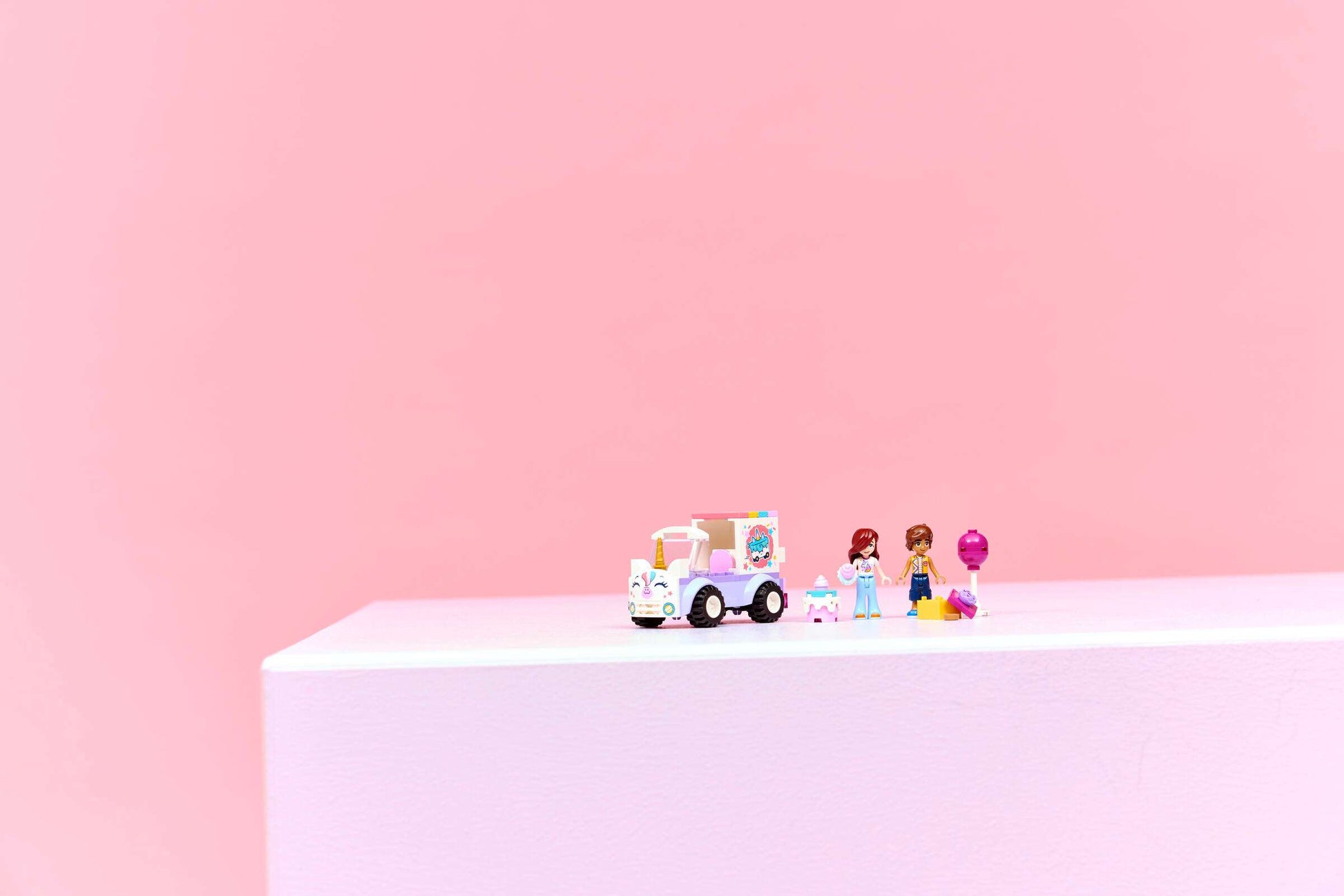 LEGO® Friends Unicorn Cake Delivery Car by Legos - Toyhouse, featuring two mini-figures, a dog, and accessories, displayed on a white surface with a pink background.