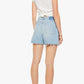 A woman stands facing away against a plain white background, wearing a white short-sleeve top and the Mother "The Extra Mile Short Fray" high-waisted denim shorts with a frayed hem, paired with black slide sandals.