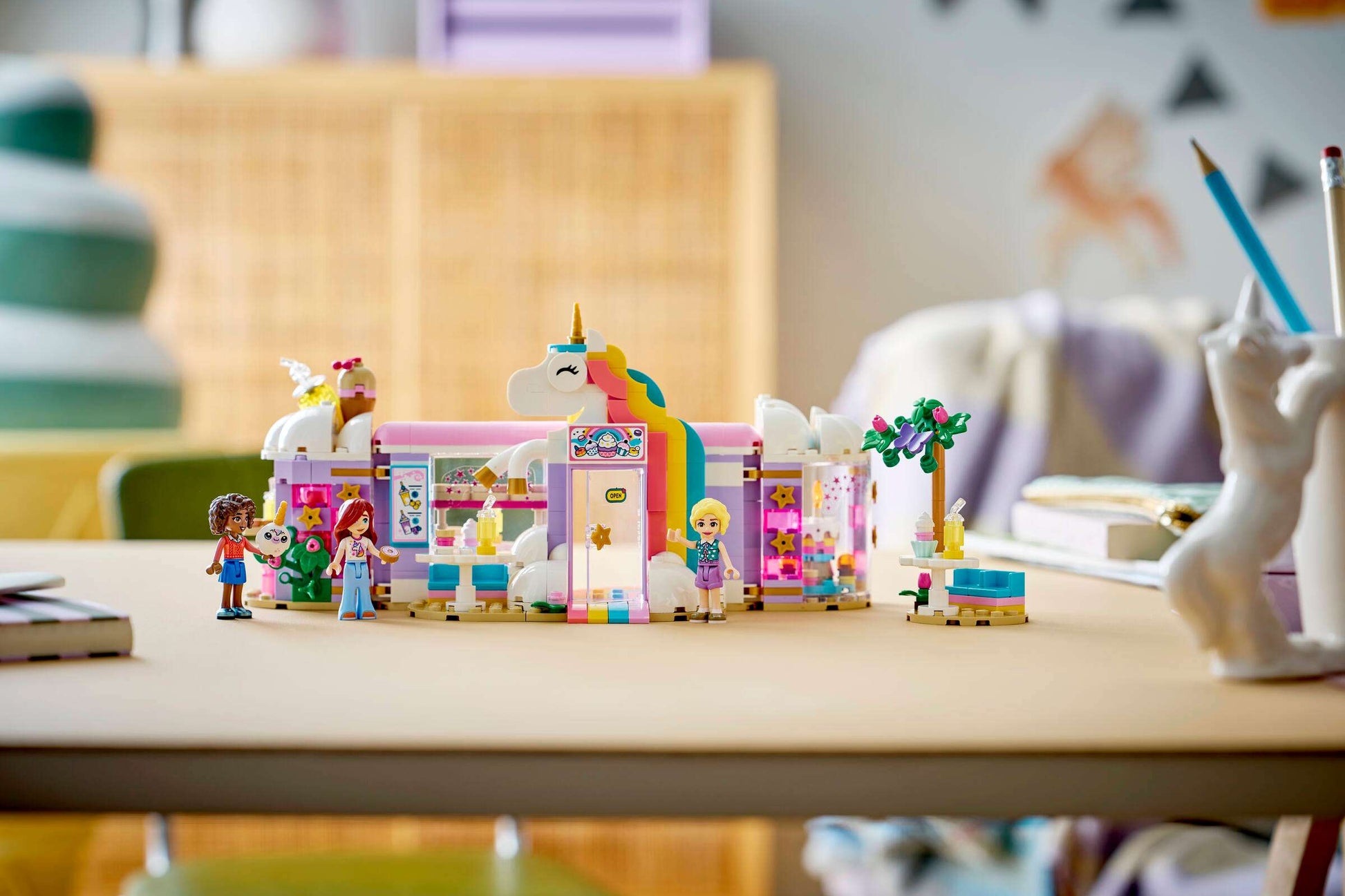 The LEGO® Friends Unicorn Dream Café by Legos - Toyhouse is shown on a table with school supplies—a vibrant building set featuring mini-figures for imaginative unicorn café play.
