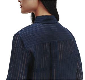 A woman is seen from the back and side wearing the TWP Boyfriend Silk Organza Shirt in navy blue sheer striped silk, styled with a relaxed fit against a white background.
