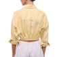 A person shown from the back wearing the Staud Lisa Linen Shirt in light yellow, styled with rolled-up sleeves and paired with high-waisted white shorts featuring an elasticated waistband.