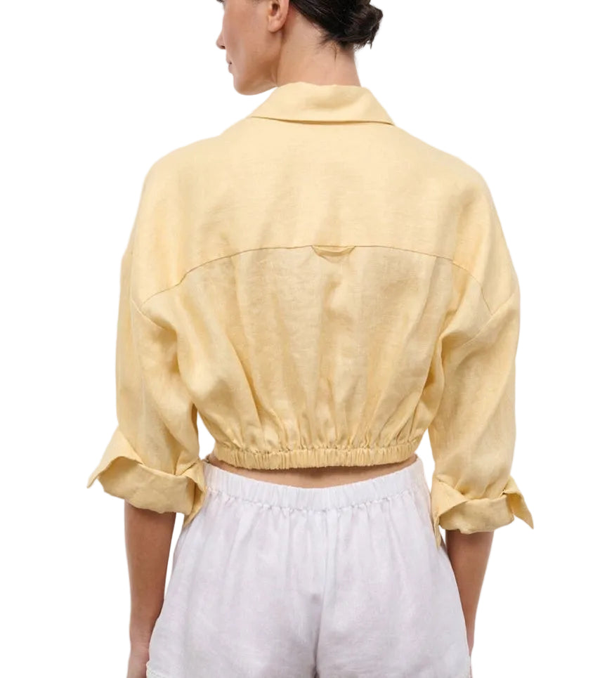 A person shown from the back wearing the Staud Lisa Linen Shirt in light yellow, styled with rolled-up sleeves and paired with high-waisted white shorts featuring an elasticated waistband.