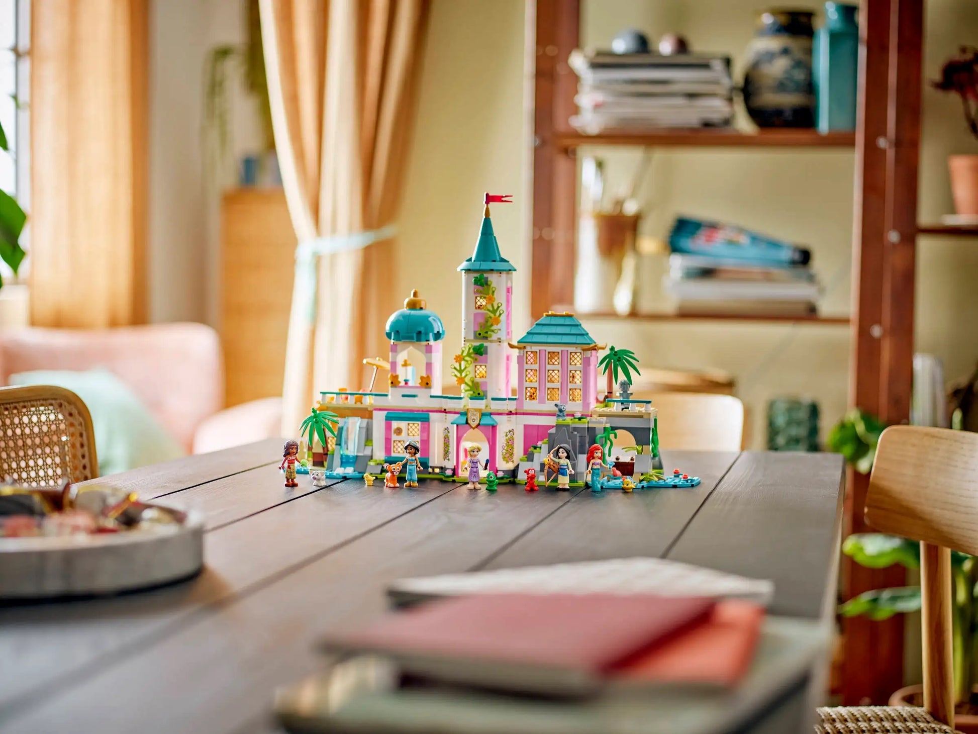 The LEGO® Disney™ Princess Castle & Royal Pets by Legos - Toyhouse is shown on a wooden table in a bright, cozy living room with bookshelves and plants in the background.