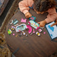 A child builds the LEGO® Disney™ Minnie's Pet Hotel from Legos - Toyhouse on a wooden table as an adult points to instructions on a nearby tablet.