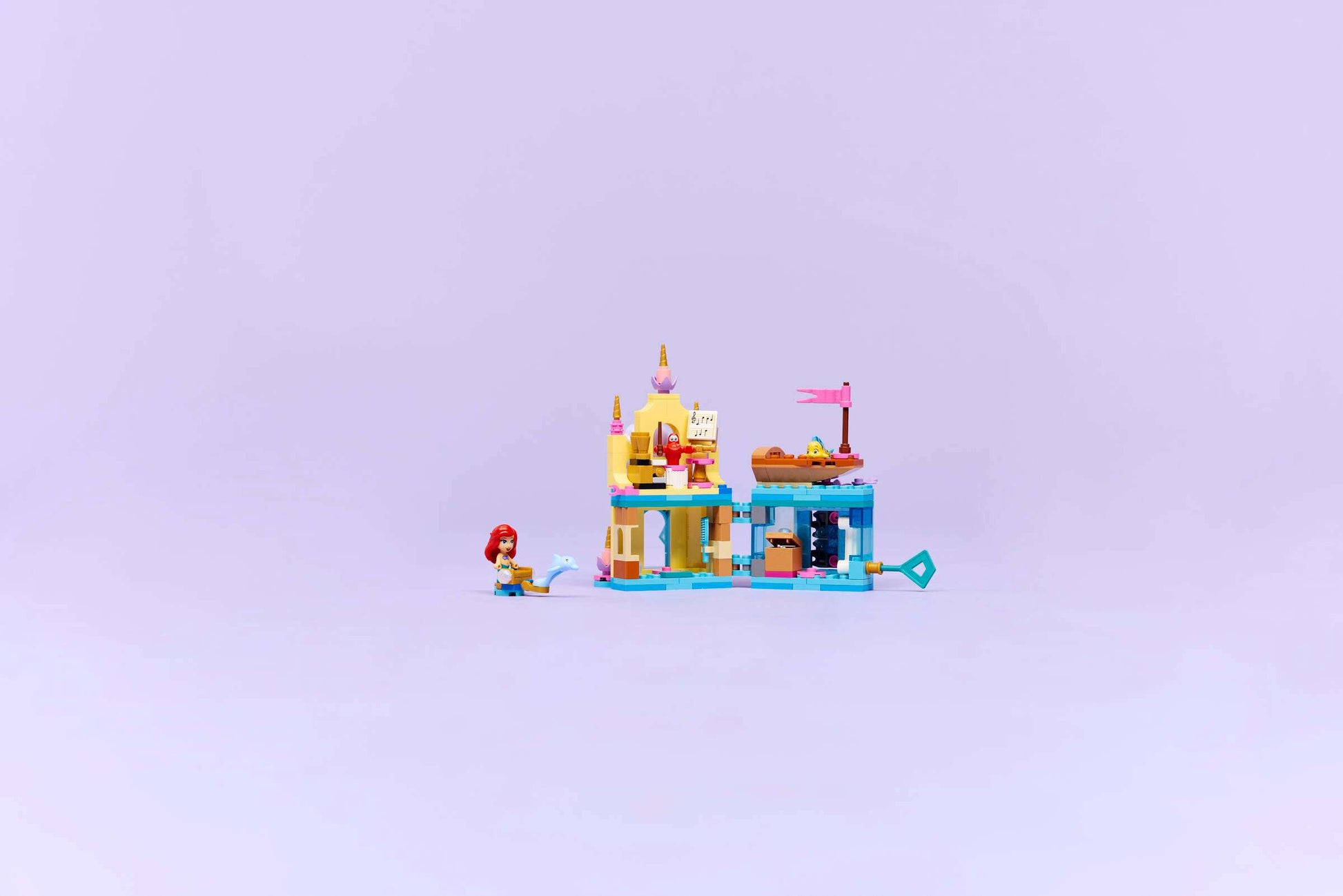 The LEGO® Disney™ Ariel's Magical Mini Palace by Legos - Toyhouse is a colorful, castle-like building toy for kids, featuring a red-haired mermaid figure and accessories, displayed on a plain light purple background.