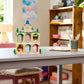 The LEGO® Disney™ Mini Belle & Tiana with Castle by Legos - Toyhouse is displayed on a gray table in a bright, tidy room with plants, shelves, and stationery.