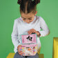 A young girl sits and looks down at an open Floss and Rock Rainbow Fairy Oval Shape Jewelry Box, featuring colorful patterns and whimsical artwork, set against a green background.