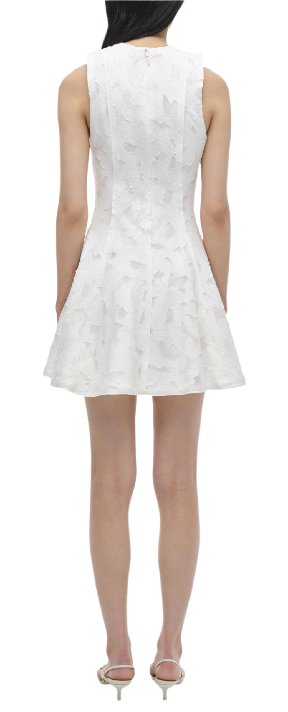 Viewed from the back, the person is wearing the Simkhai Sylvia Mini Dress, a sleeveless design featuring a flared skirt and textured pattern. Ideal for warm days, this jacquard piece exudes effortless elegance.