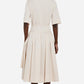 A person faces away, wearing the CO Short Sleeve Belted Cotton Poplin Dress with a collared neckline and pleated skirt—styled with flat sandals for an effortless summer essentials look.