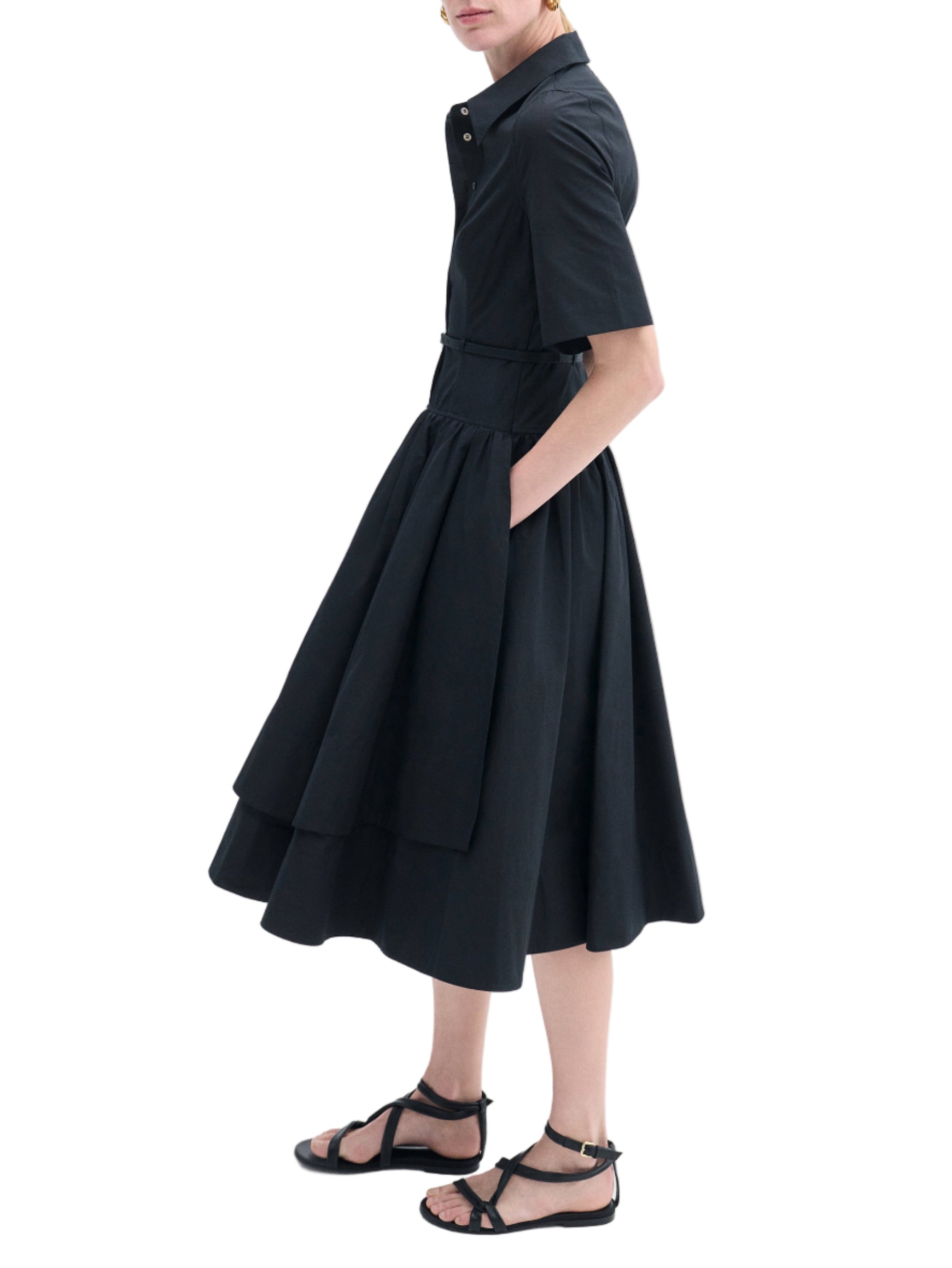 Someone wearing the CO Short Sleeve Belted Dress, featuring a black cotton poplin midi skirt and black sandals, stands against a white background.