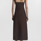 A person faces away, wearing the CO Bustier Cut Dress—a sleeveless dark brown cotton poplin dress with thin straps—paired with flat shoes, set against a plain white background.