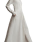 A woman wearing TWP's Main Street After Midnight long sleeve white collared maxi dress with side pockets and flat sandals stands against a white background.