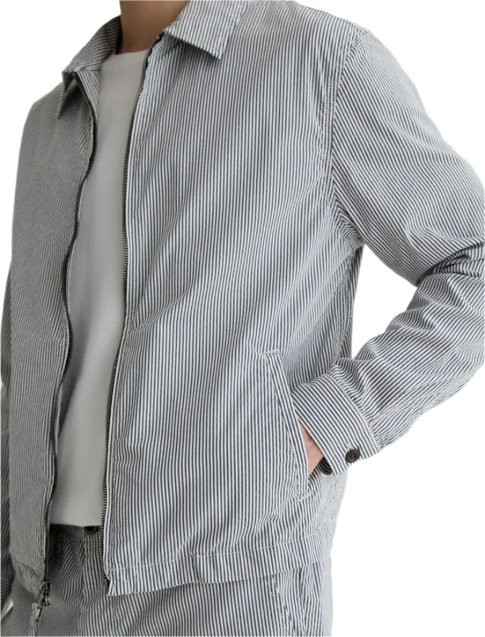 Model wears the AG Jeans Philip Zip Jacket with matching pants over a plain white shirt, shown from shoulder to hip with hands in pockets.