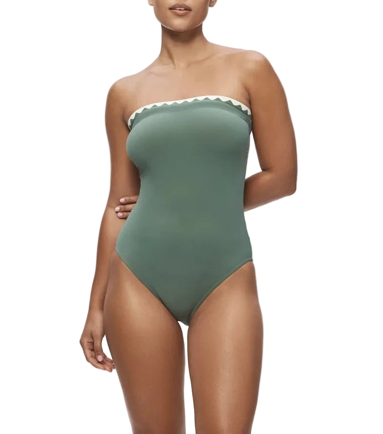 A woman models the Karla Colletto Lia Bandeau One Piece in sage green with white scalloped rickrack trim along the top edge, posed against a white background.