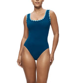 A woman models the Karla Colletto Lia Round Neck One Piece, a blue rickrack-trimmed swimsuit, against a white background—chic swimwear ideal for relaxing after a swim.