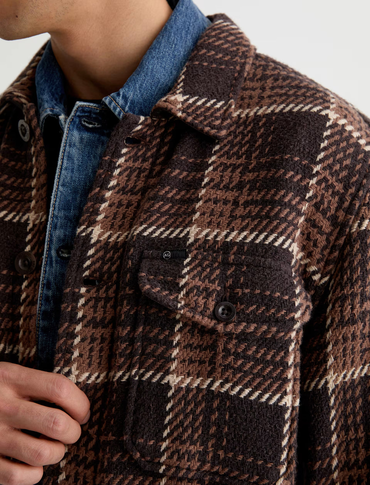 A person wearing a brown and tan houndstooth Grant Overshirt layered over a denim jacket.