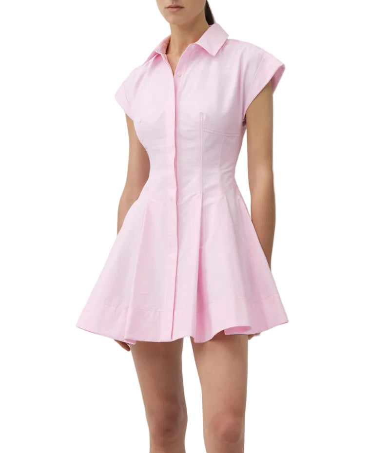A woman wears the Simkhai Clemmie Mini Dress, a light pink cotton piece with cap sleeves, a collared neckline, and a flared skirt.