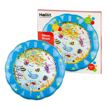A blue plastic Wave Drum by Crocodile Creek features a textured rim, colorful beads inside, and sea creature decorations to create soothing ocean wave sounds. Shown beside its packaging labeled "Wave Drum.
