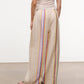 A person wearing Staud's Mateo Linen Pant in relaxed fit with beige vertical multicolored stripes and a light sleeveless top stands on a smooth floor, seen from behind—a stylish warm-weather pick.