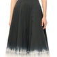 A person stands against a plain background in Staud's Wells Dress, a sleeveless black cotton poplin piece with a white gradient hem, complemented by chic white sandals for an elegant touch.