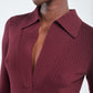 Woman wearing the Maria McManus Single Button Polo, a ribbed, slim-fitting deep burgundy top with long sleeves and a V-neckline; partial view of her face and upper body.