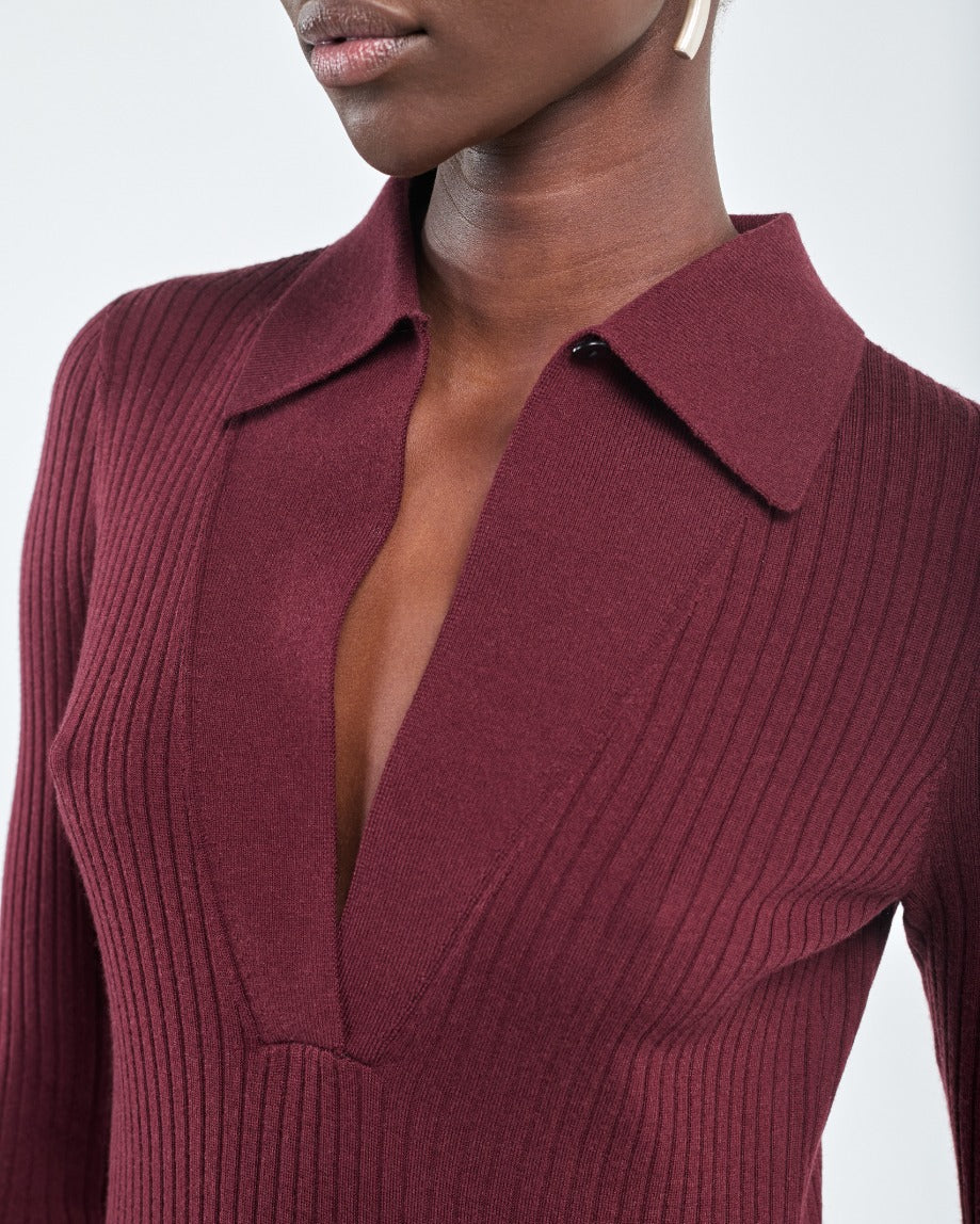 Woman wearing the Maria McManus Single Button Polo, a ribbed, slim-fitting deep burgundy top with long sleeves and a V-neckline; partial view of her face and upper body.