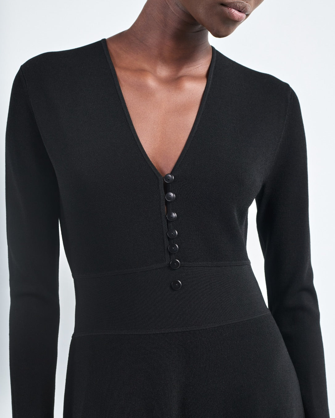 A person wearing the Maria McManus Button Front Dress, featuring long sleeves, a deep V-neck, and elegant corozo nut buttons down the front.