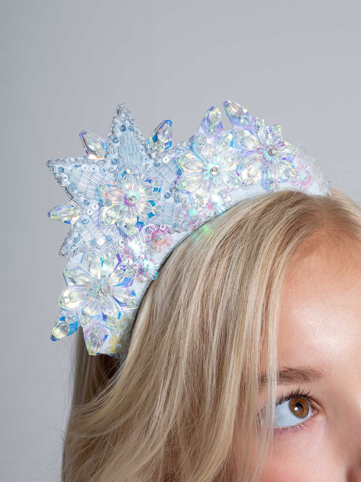 A close-up of a person with blonde hair wearing the Tutu du Monde Snow Queen Tiara, a white beaded headband adorned with large, iridescent floral designs that evoke the look of a delicate flower tiara.