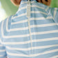 A close-up of a child wearing The Beaufort Bonnet Company's Baby Boys' Price Pool Romper, a blue and white striped swim romper featuring a white back zipper.