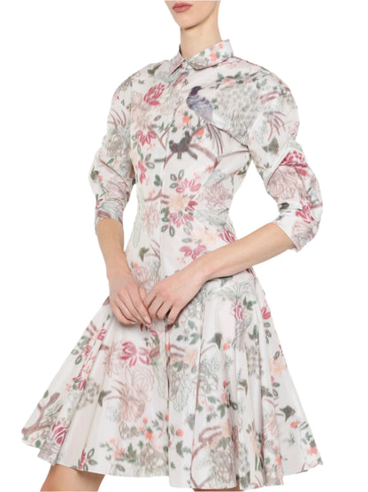 A person elegantly dons a white, floral-patterned Mini Shirtdress by Prabal Gurung, featuring three-quarter sleeves and a flared skirt for a stylish yet comfortable look.