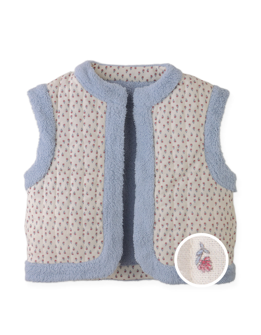 The Girls’ Eulalia Floral Reversible Vest from Gingersnaps features a sleeveless quilted design with blue sherpa trim and a ditsy floral print, highlighted by an inset showing a small embroidered flower detail on the fabric.