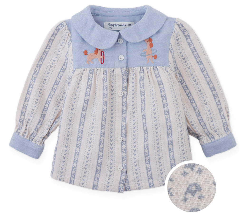 The Gingersnaps Baby Girls’ Hester Striped Floral Blouse features blue and white vertical stripes, a blue collar and cuffs, front button closure, and embroidered dogs playing with hoops on the chest. An inset highlights the textured fabric.