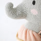 Close-up of Eloise the Elephant - Little 13" by Cuddle + Kind, a knitted gray stuffed animal with a raised trunk, black eye, pink cheek, and peach outfit—an adorable birthday gift option.