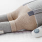 Close-up of Cuddle + Kind’s “Noah the Dog - Regular 20" plush toy, featuring beige, gray, and blue sections, resting on a white textured surface. #NoahBirthday.