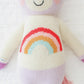 Zoe the Unicorn - Little 13" by Cuddle + Kind is a magical knitted stuffed toy with a cream-colored body, pastel purple accents, and a rainbow torso, resembling a unicorn, shown on a white surface.