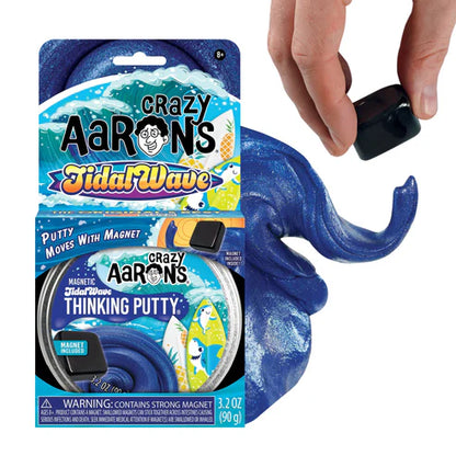 A hand hovers a magnet above Crazy Aarons Tidal Wave Magnetic Storm Thinking Putty, making the blue, magnetic putty swirl and shift. Both the product packaging and sensory toy are visible together.