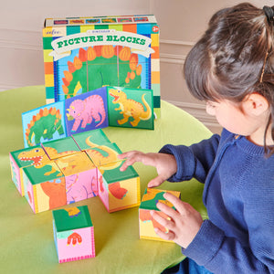 A child arranges colorful Eeboo Dinosaur Picture Blocks on a table, with the product box labeled "Dinosaur Picture Blocks" visible in the background.