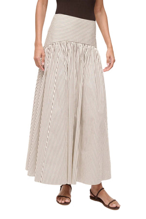 A person wearing a black sleeveless top, brown sandals, and the Staud Procida Skirt—a cream, high-waisted maxi skirt with black vertical stripes and a hidden back zipper.