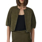 A woman wears the Simkhai Austyn Short Sleeve Suede Jacket in olive green, featuring a concealed front zipper, over a black top and matching skirt; shown from shoulders to hips.