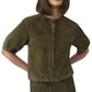 A woman wears the Simkhai Austyn Short Sleeve Suede Jacket in olive green, featuring a round neckline, paired with a matching skirt, standing with hands on her hips.