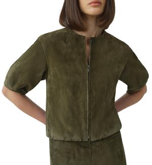 A woman wears the Simkhai Austyn Short Sleeve Suede Jacket in olive green, featuring a round neckline, paired with a matching skirt, standing with hands on her hips.