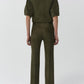 A person stands facing away, wearing the Simkhai Austyn Short Sleeve Suede Jacket in olive green with matching pants and black shoes, set against a plain light background.