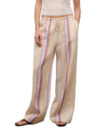 A person wears Staud's Mateo Linen Pant—relaxed fit, beige with vertical rainbow stripes—paired with a white sleeveless top and sandals, making it a perfect warm-weather look.