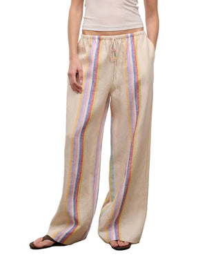 A person wears Staud's Mateo Linen Pant—relaxed fit, beige with vertical rainbow stripes—paired with a white sleeveless top and sandals, making it a perfect warm-weather look.